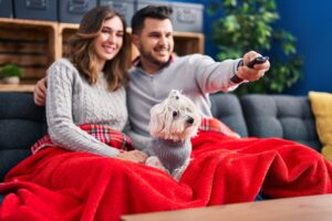 Man and woman watching movie sitting on sofa with dog at home